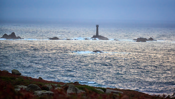 Longships mist This landscape photograph captures the misty coast of Cornwall in the early evening during autumn. The main subject is Longships mist, with the Longships lighthouse prominently emerging from a cluster of rocky outcrops in the sea. The coastline, featuring rugged terrain and patches of vegetation, can be seen in the foreground, while the waves of the Atlantic Ocean reflect the dimming light. The Longships lighthouse serves as a vital landmark for maritime navigation along the Cornish coast, and the muted tones of the water and sky highlight the atmospheric conditions characteristic of autumn evenings in Cornwall.